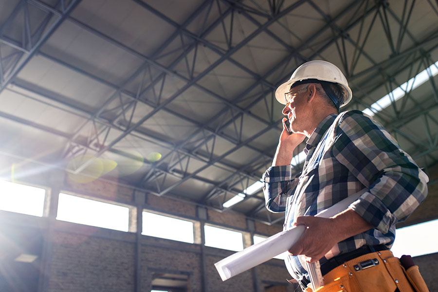 Specialized Business Insurance - View of Contractor Talking on the Phone Holding Construction Plans at a Building Jobsite